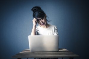 パソコンを見ながらブログが書けなくて落ち込む女性